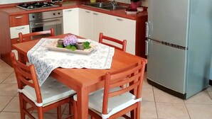 A compact kitchen with a dining table, chairs, a refrigerator, a stove, and a sink. - TIGLI APARTMENT NEAR VENICE (Noale)