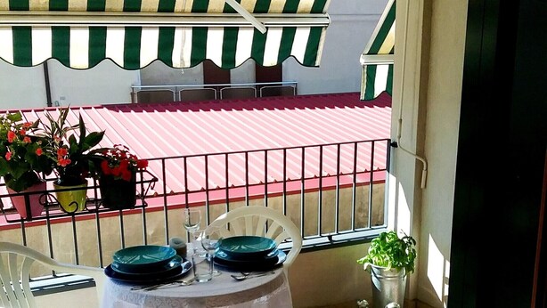 A balcony with a table set for two, potted plants, and a red and white striped awning. - TIGLI APARTMENT NEAR VENICE (Noale)
