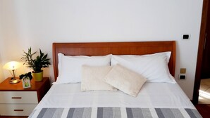 A neatly made bed with white linens and two pillows, a bedside table with a lamp and a potted plant, and a wooden headboard. - TIGLI APARTMENT NEAR VENICE (Noale)
