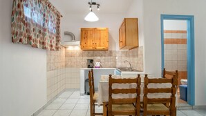A kitchen with wooden cabinets, a tiled backsplash, a sink, and a dining table with chairs. - Two-Bedroom Apartment (5-6 Adults) Semi Basement, near center. (PARIKIA PAROS GREECE)