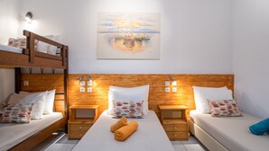 A room with a bunk bed, two single beds, wooden headboard, bedside tables, and a painting of boats on water. - Two-Bedroom Apartment (5-6 Adults) Semi Basement, near center. (PARIKIA PAROS GREECE)