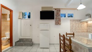 A compact kitchen with a refrigerator, a TV mounted above it, and a dining area with a glass table and wooden chairs. - Two-Bedroom Apartment (5-6 Adults) Semi Basement, near center. (PARIKIA PAROS GREECE)