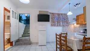 A compact kitchen with a built-in refrigerator, a dining table with chairs, a staircase leading to an upper level, and a TV mounted on the wall. - Two-Bedroom Apartment (5-6 Adults) Semi Basement, near center. (PARIKIA PAROS GREECE)