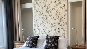 Habitació d'hotel ben organitzada amb un llit, dues taules de nit, una estora vermella i un paper pintat floral.