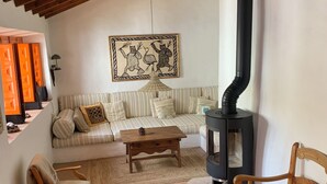 Uma sala de estar acolhedora com teto alto, um sofá, duas cadeiras de madeira, uma pequena mesa de centro e uma lareira a lenha.