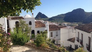 Um edifício branco com telhado em cerâmica, parede de pedra e vista para uma montanha.