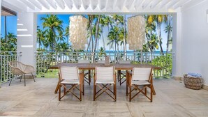 A dining area with a view of palm trees and the sea, featuring a wooden table and chairs, a wicker chair, and a woven basket. - Stunning Luxury Oceanfront House, Modern,  Best of The Best Location  (Las Terrenas)
