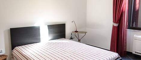 A bedroom with a bed, a bedside table, a lamp, and a window with curtains.