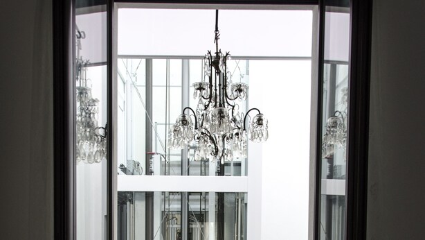A view through a glass door into a balcony area with a chandelier, potted plants, and a modern building in the background. - Beautiful furnished apartment in the center (int. 1) (brindisi)