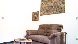 A brown sofa with a small round table in front of it, a framed picture on the wall, and a large patterned artwork above the sofa. - Beautiful furnished apartment in the center (int. 1) (brindisi)