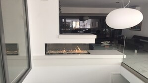 Una sala de estar moderna con chimenea empotrada, un ventanal grande y una lámpara colgante.
