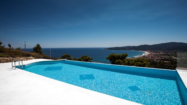 Una piscina con vista despejada al mar y un pueblo costero al fondo.