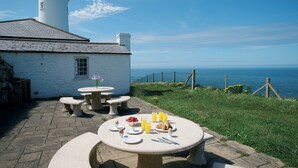 A dining table set with plates, glasses, and cutlery, overlooking a coastal view with a lighthouse in the background.