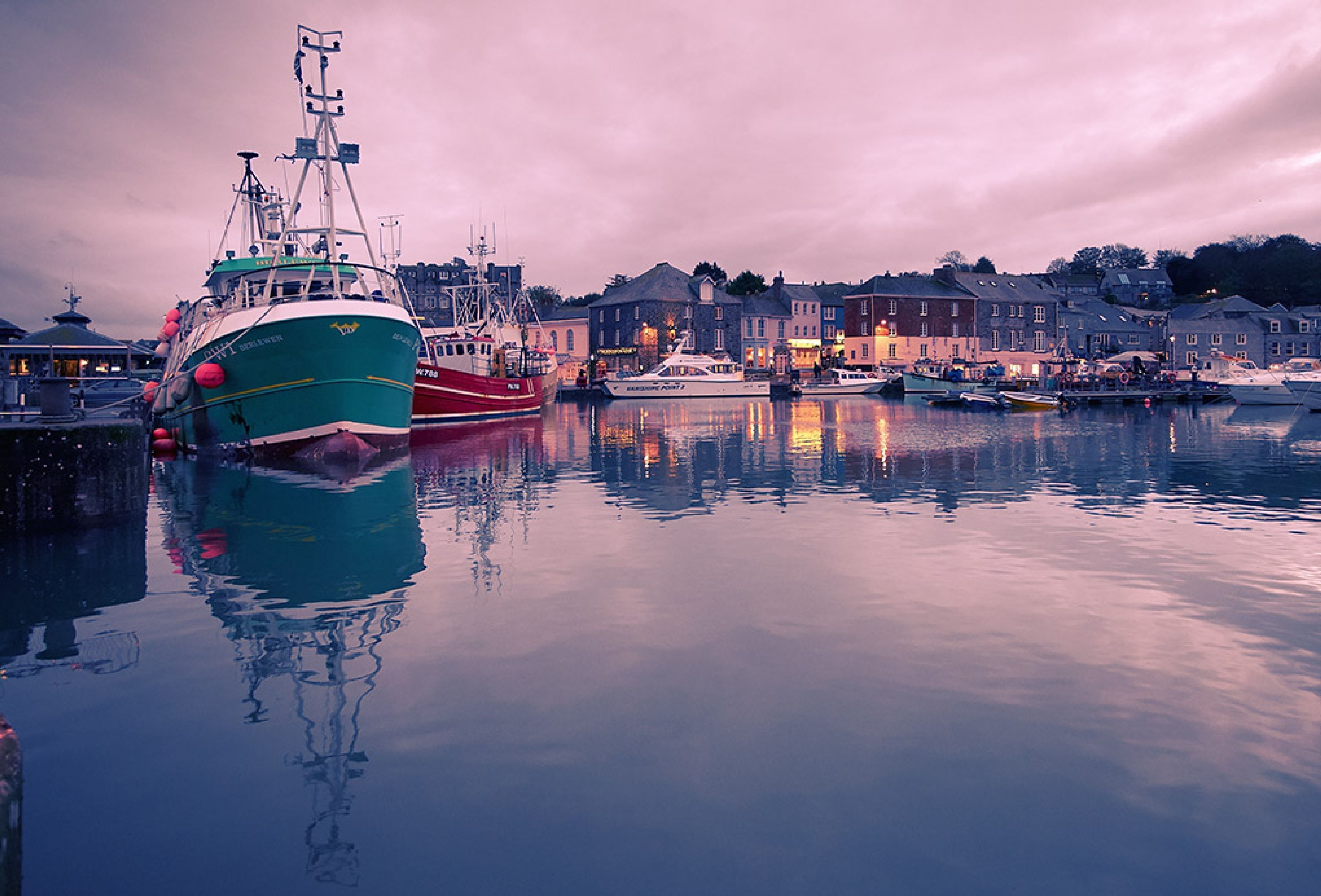 A harbor with boats docked, calm water, and buildings along the shore.
