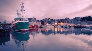 A harbor with boats docked, calm water, and buildings along the shore.