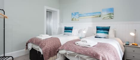 A hotel room with two beds, a nightstand, a lamp, and artwork on the wall.