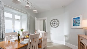 A dining area with a wooden table, white chairs, a wall clock, and a framed picture.