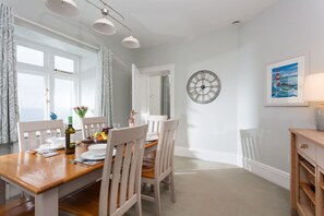A dining area with a wooden table, white chairs, a wall clock, and a framed picture.