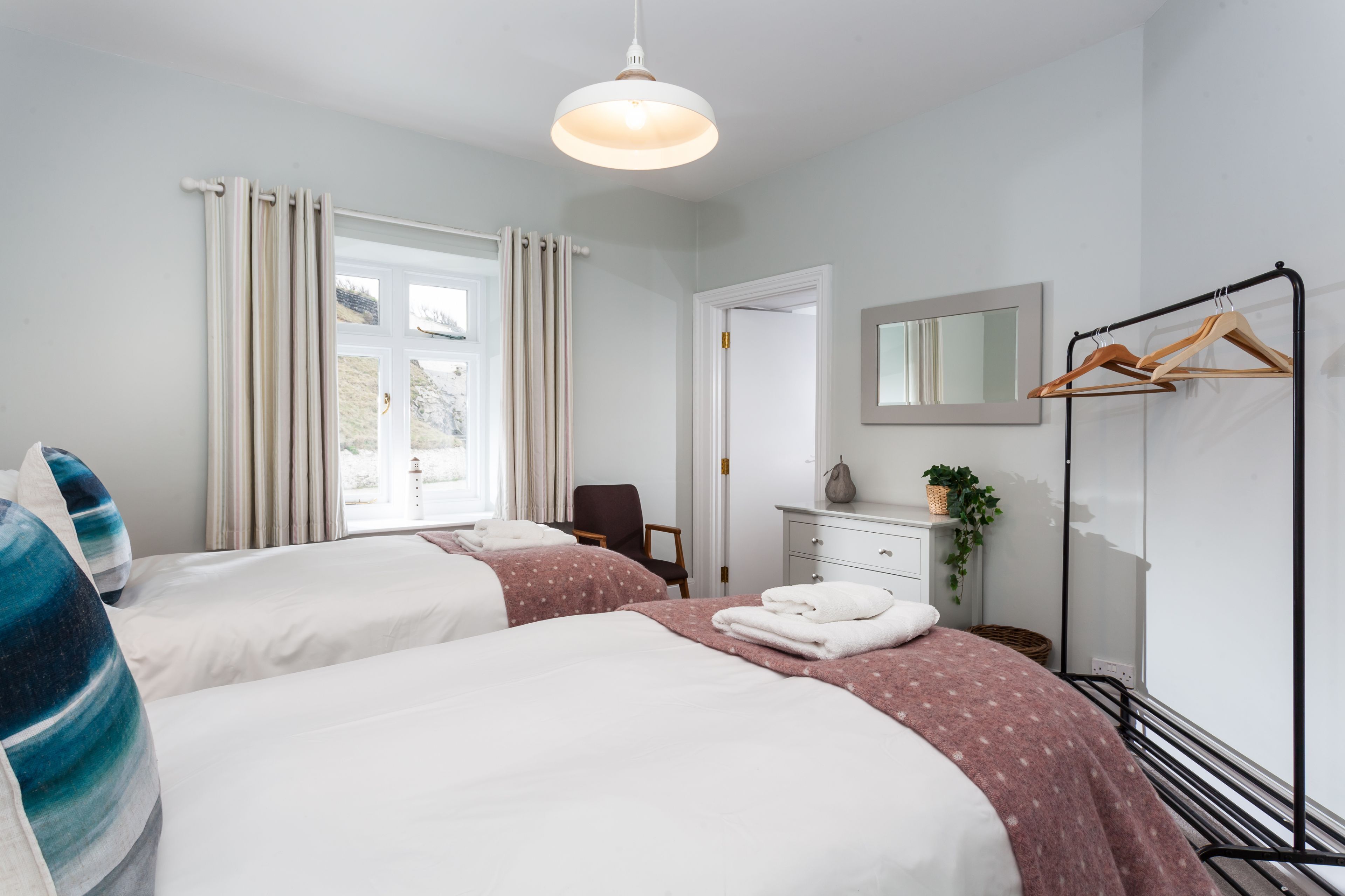 A hotel room with two beds, a dresser, a mirror, a coat rack, and a window with curtains.