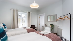 A hotel room with two beds, a dresser, a mirror, a coat rack, and a window with curtains.