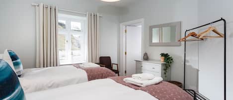 A hotel room with two beds, a dresser, a mirror, a coat rack, and a window with curtains.