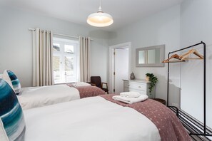 A hotel room with two beds, a dresser, a mirror, a coat rack, and a window with curtains.