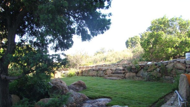 A stone wall surrounding a grassy area with a small water feature.