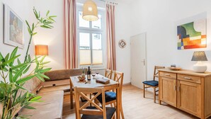 Un área de comedor con una mesa, sillas, un sofá, una lámpara, un reloj y un cuadro en la pared.