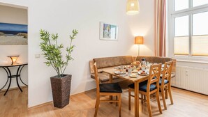Un comedor con mesa de madera, sillas, una banca, planta en maceta, lámpara, un cuadro en la pared y una ventana con persianas.