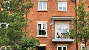 A two-story brick building with a green door, windows, and a balcony with outdoor furniture.