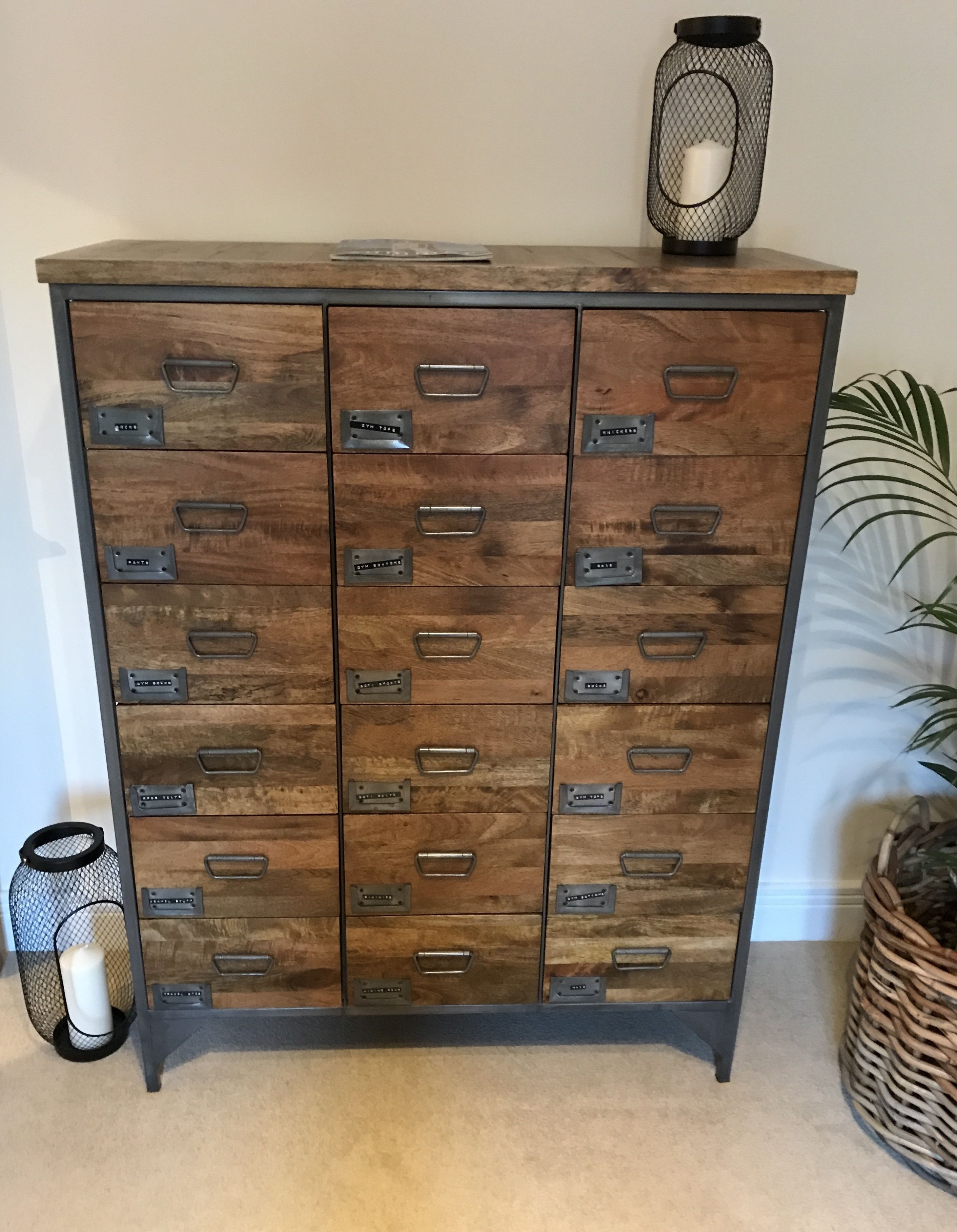 A wooden cabinet with multiple drawers and metal handles, accompanied by a small black basket and a decorative vase.
