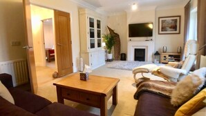 A living room with a sofa, a coffee table, a fireplace, a television, and a door leading to another room.