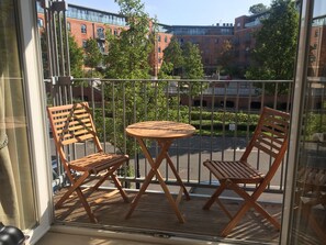 En balkon med to træstole og et rundt bord, med udsigt over en parkeringsplads og bygninger.