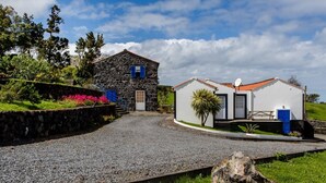 A stone house with a gravel driveway, a white building with a red roof, and a stone wall with a blue door. - Casa da Avó - Quinta da Ribeira da Urze (Prainha de cima)