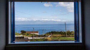 A view from a window with a white frame, overlooking a coastal area with houses, a road, and a clear sky. - Casa da Avó - Quinta da Ribeira da Urze (Prainha de cima)