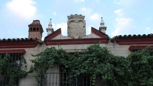 Un edificio con un escudo decorativo, un balcón con barandilla de hierro y una chimenea de ladrillo.