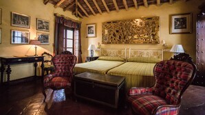 Una habitación con techo de madera, una cama con ropa de cama verde, dos sillones de cuadros, una mesita y cuadros enmarcados en las paredes.