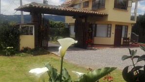 A two-story house with a tiled roof, a gated entrance, and a driveway. - Hospederia El Portal de las Flores (Chia)