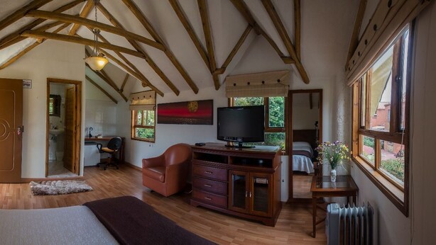 A bedroom with a wooden ceiling, a bed, a TV, a desk, and a window. - Hospederia El Portal de las Flores (Chia)