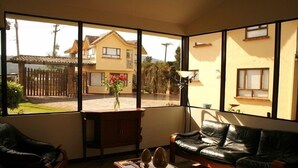 A living room with a sofa, a coffee table, and a view of a yellow house through large windows. - Hospederia El Portal de las Flores (Chia)