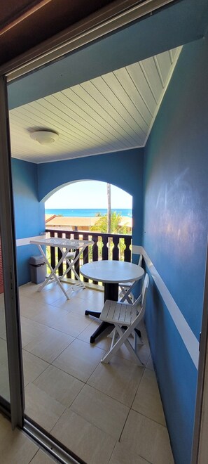 A balcony with a table and chairs, a trash bin, and a view of the ocean. - Studio Vue mer des Caraïbes, un Petit Coin de Paradis (Sainte Anne)