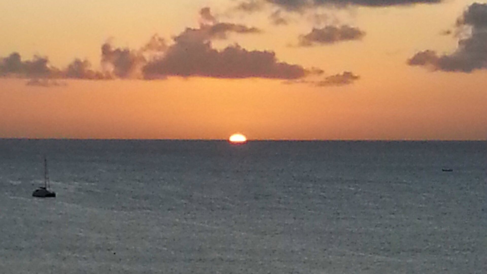 Un coucher de soleil sur une mer calme, avec un seul bateau à l'horizon.