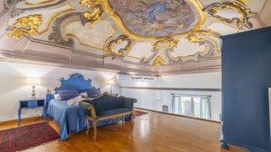 Quarto com cama azul, teto ornamentado e vista da cidade.