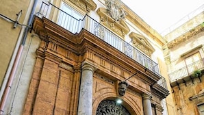 Um edifício histórico com uma grande entrada em arco, colunas e uma varanda com grades.