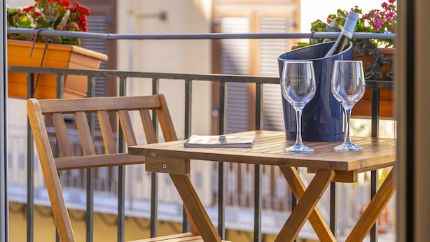 Uma mesa de madeira com duas taças de vinho e uma garrafa numa varanda com guarda.