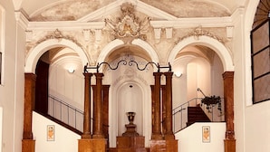 Uma escadaria imponente com colunas ricamente decoradas, uma fonte central e um teto ornamental.