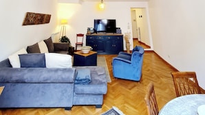 Uma sala de estar com pé direito alto, uma televisão, um sofá, uma poltrona azul e uma mesa de jantar.