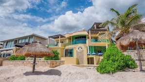 Una propiedad frente a la playa con una casa grande que cuenta con varios balcones, piscina y jardines tropicales.