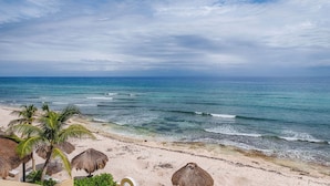 Una playa con cielos despejados, mar tranquilo y sombrillas de paja.