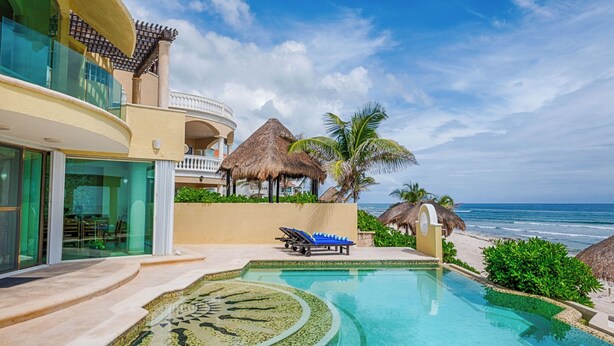 Un resort con piscina, vista a la playa y una estructura de techo de paja.